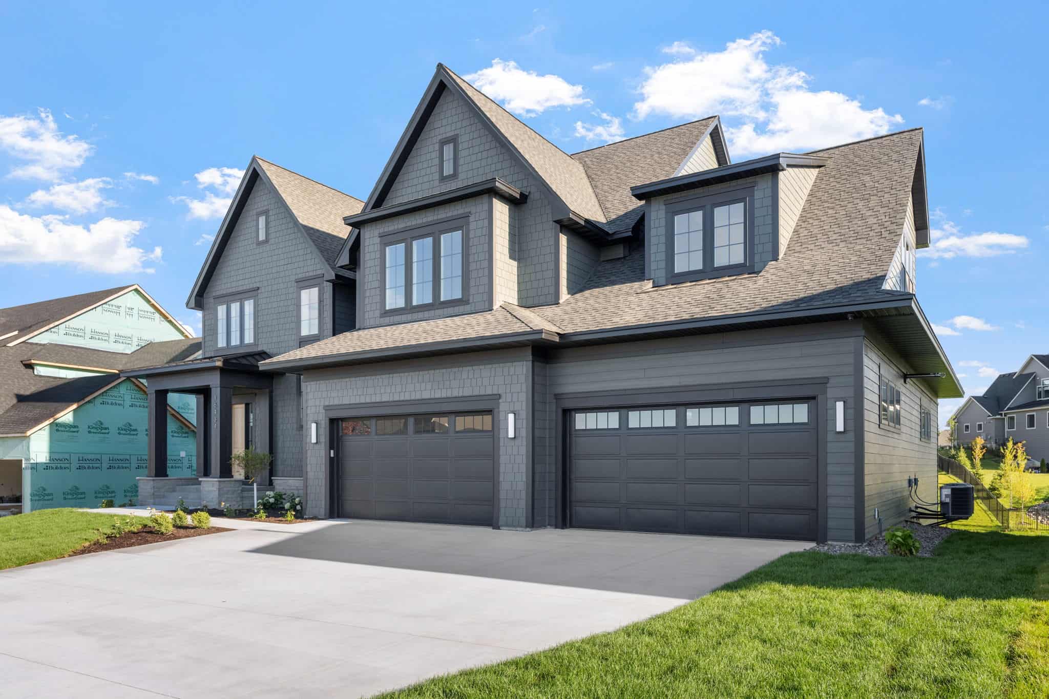 Modern gray house with triple garage and landscaped yard, home exterior design.