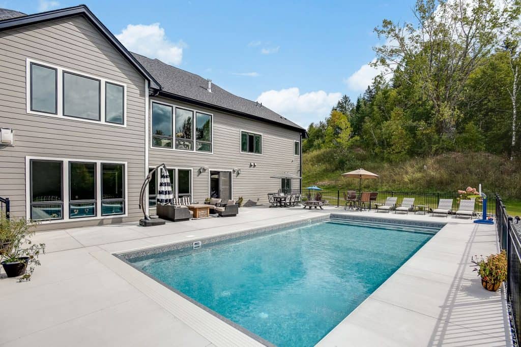 Modern residential backyard with a concrete pool deck and outdoor seating area.