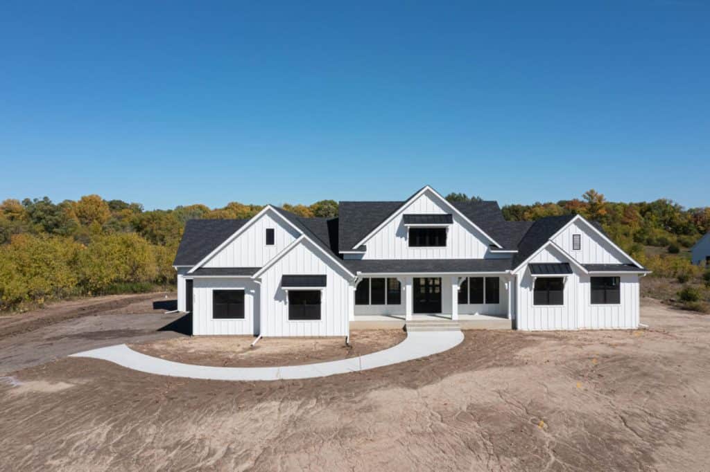 Modern white house with black roof and concrete pathway, under clear blue sky.