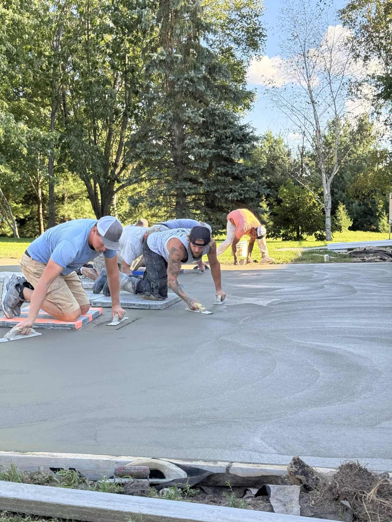 Workers smoothing freshly poured concrete driveway outdoors