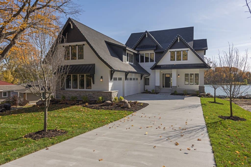 Elegant modern house with concrete driveway, landscaped yard, and lake view.
