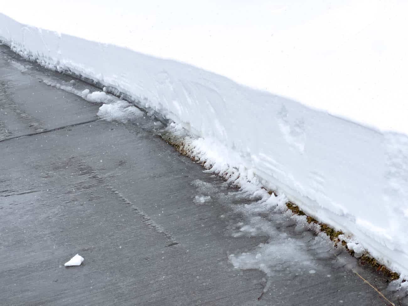 Shoveled sidewalk beside tall snowbank in winter